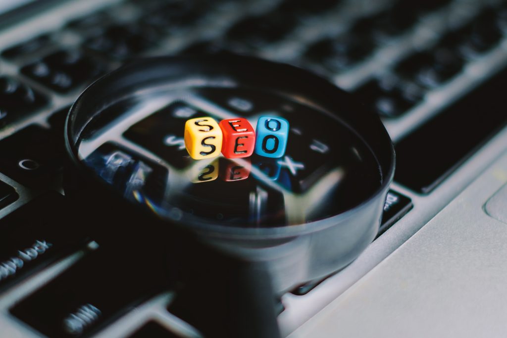 A three letter "SEO" on the magnifying glass and computer keyboard background, Search engine optimization concept (added color filter)