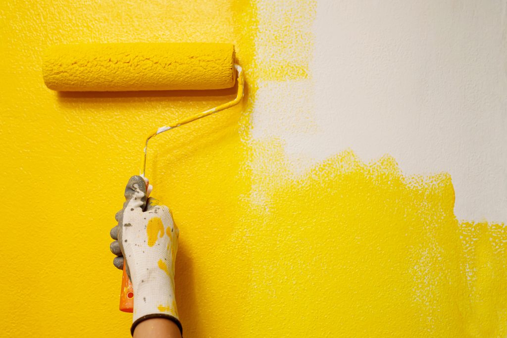 Roller Brush Painting, Worker painting on surface wall Painting apartment, renovating with yellow color paint. Leave empty copy space white to write descriptive text beside.