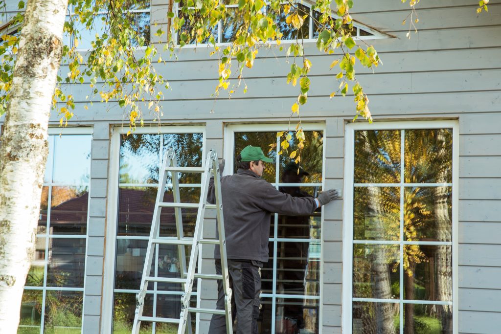 The worker makes painting of the facade of the wooden frame house after installation of windows. Construction worker thermally insulating eco wooden frame house with wood fiber plates